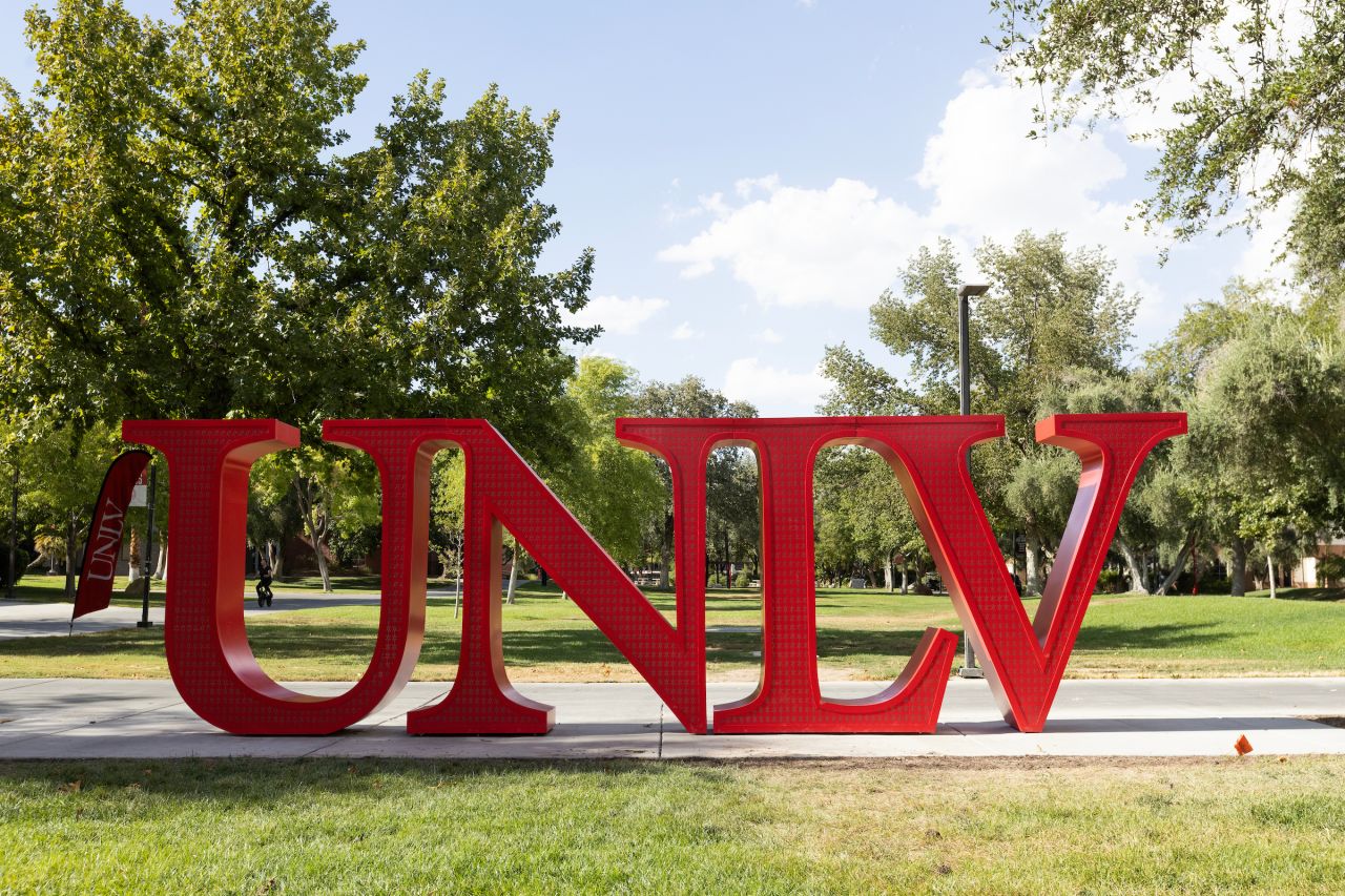 Large crimson UNLV letters surrounded by trees and campus lawns